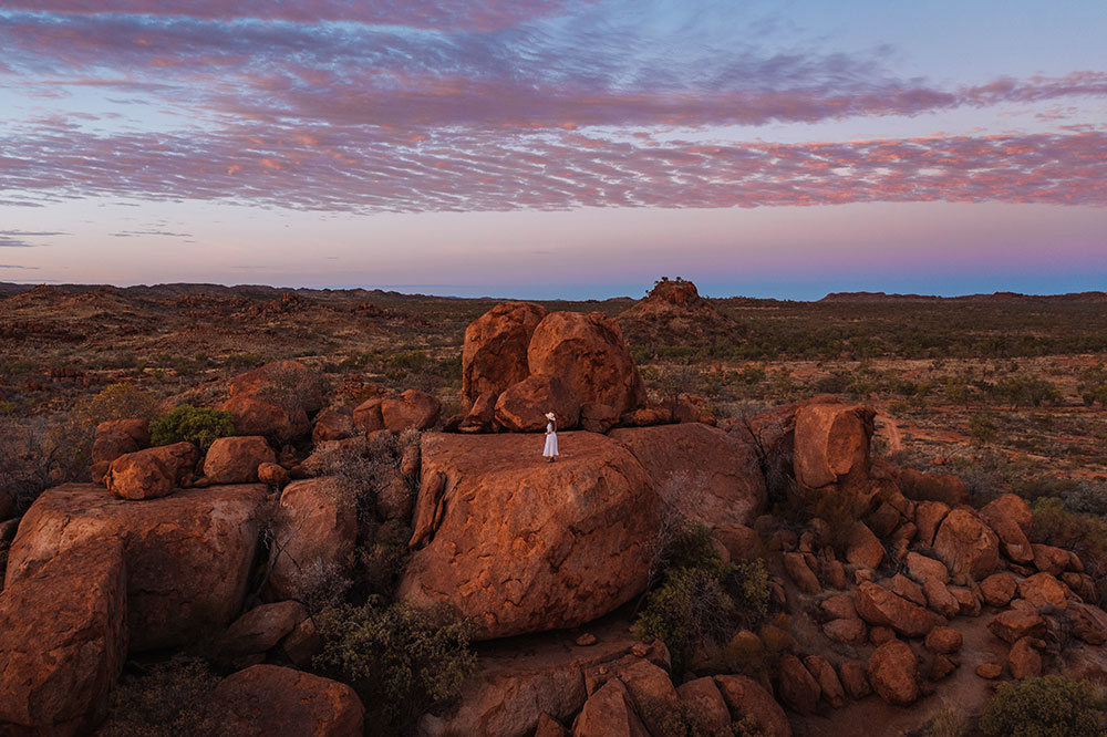 Woman in white dress standing on large rock in Outback Queensland.