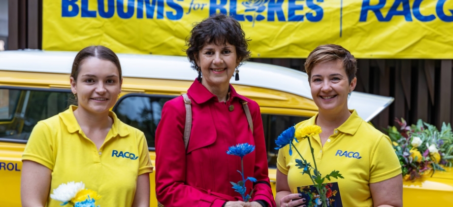 RACQ staff standing with lady standing in front of blooms for blokes sign with flowers
