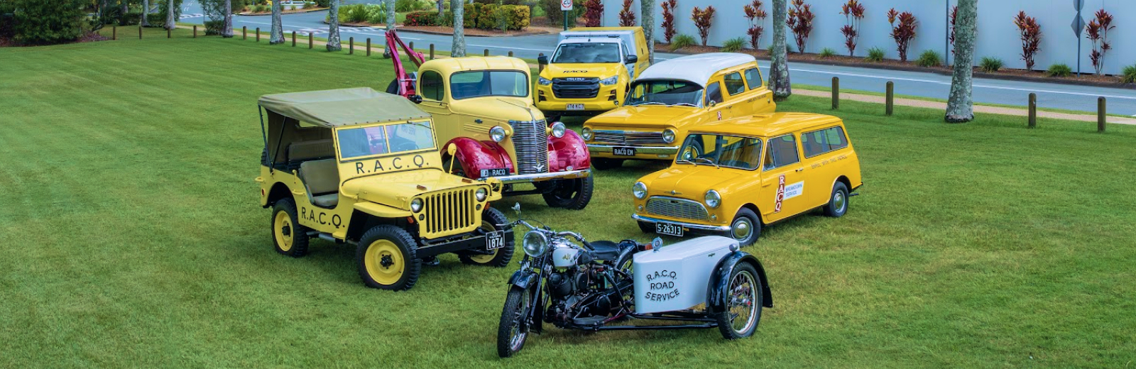 A group of historic RACQ vehicles from different eras on a large green lawn