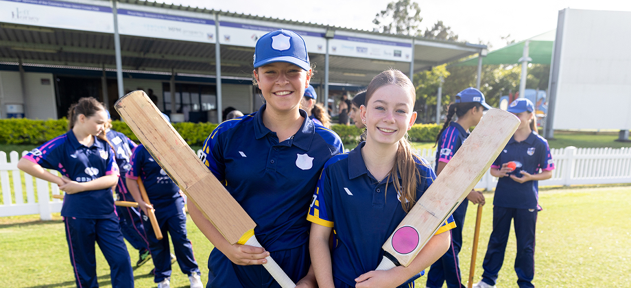 two girls smiling holding cricket bats