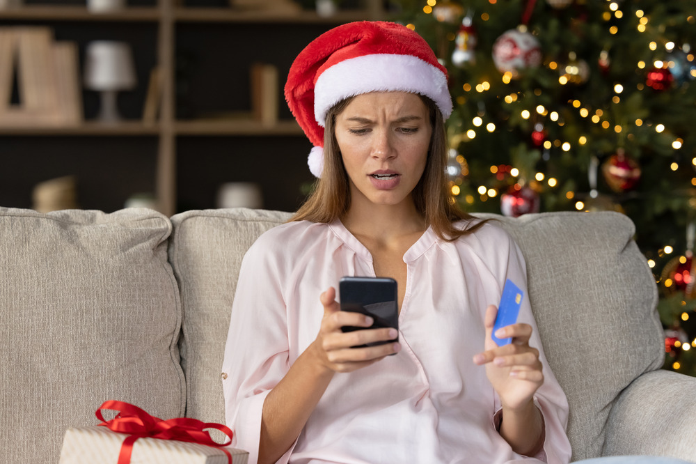 Woman in santa hat looking worried at phone and credit card
