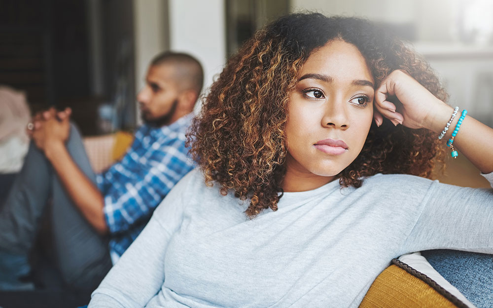 Black woman on one end of couch and black man at the other end. the look like they've had a fight.