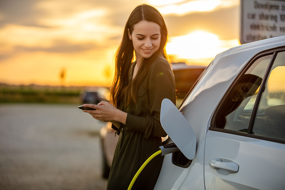 Young woman on mobile phone while EV is charging.