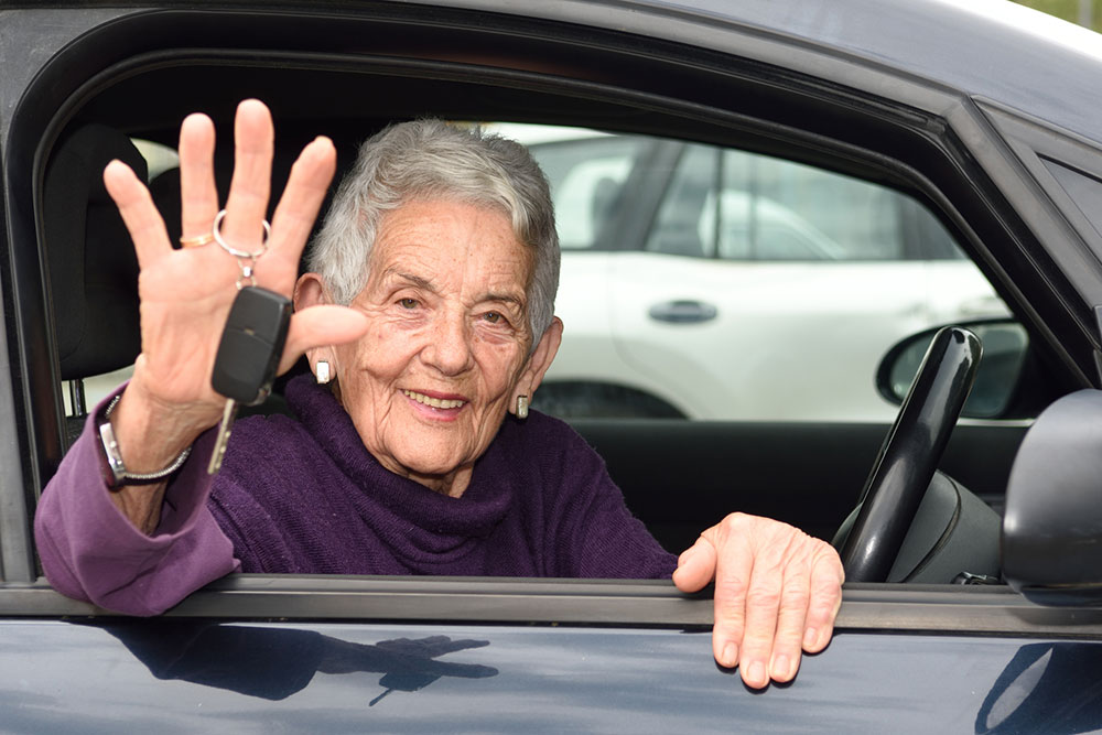 Elderly woman waving car keys while sitting behind the wheel.