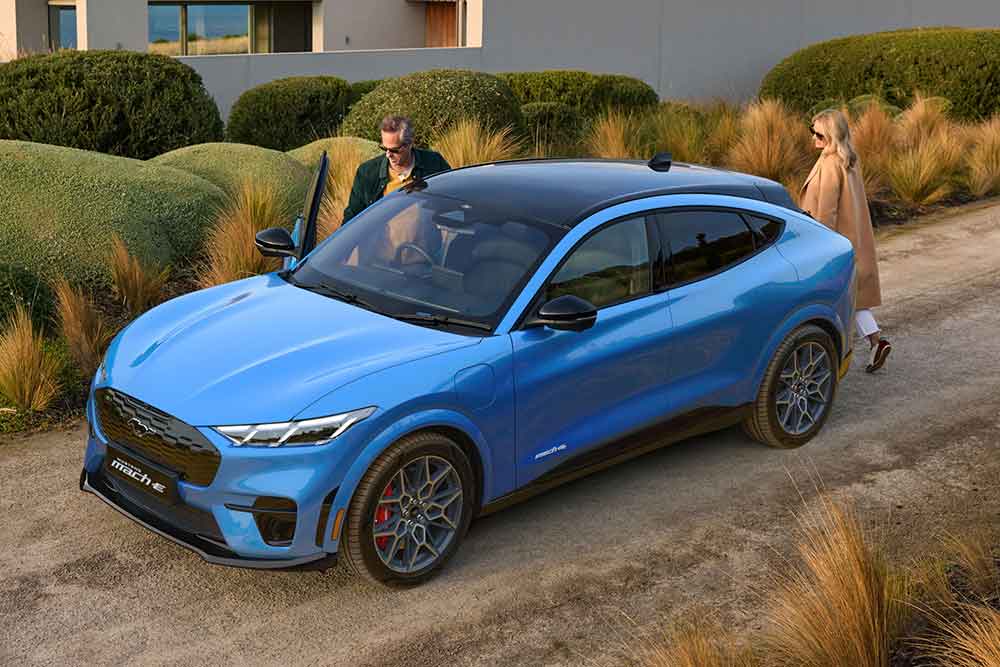 Two people beside the 2025 Ford Mustang Mach-E GT parked in a driveway.