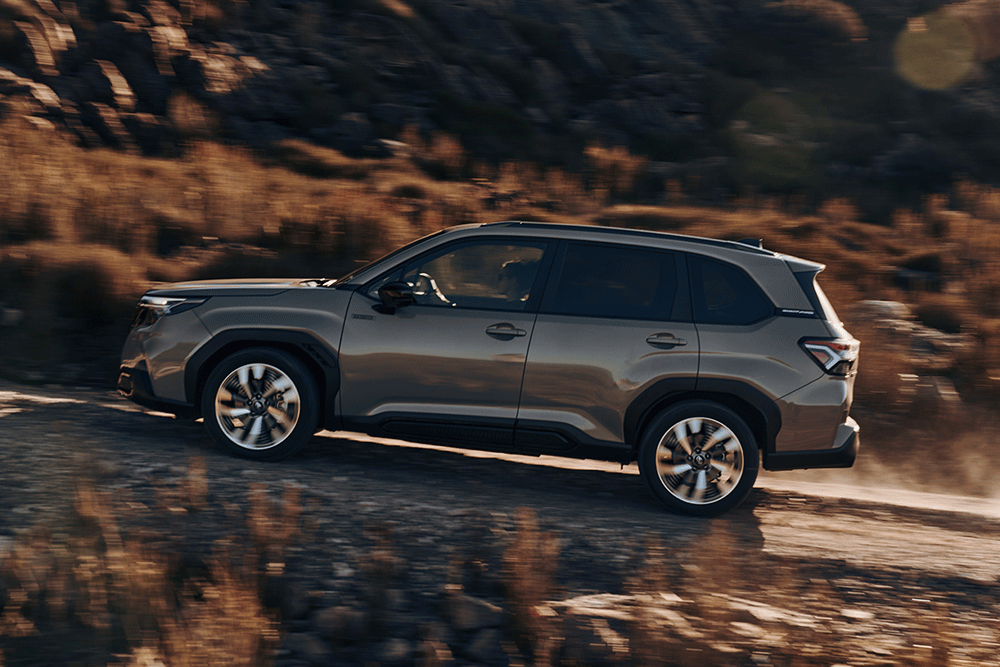 Side view of sixth-generation Subaru Forester driving up dirt road.