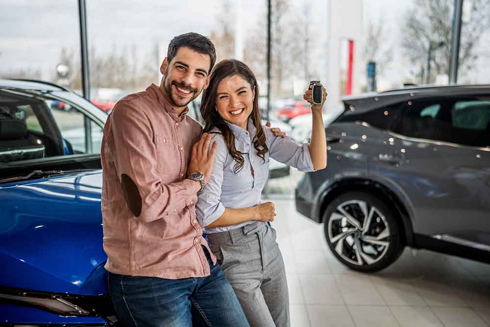 Couple with keys to a new car in showroom.
