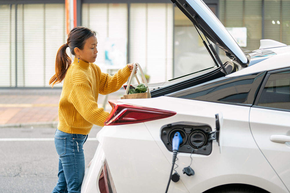 A woman loads shopping into the boat of an EV which is being recharged.