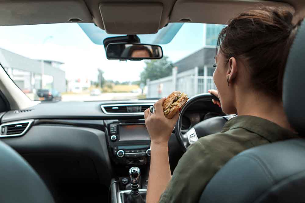 Woman driving and eating a hamburger.