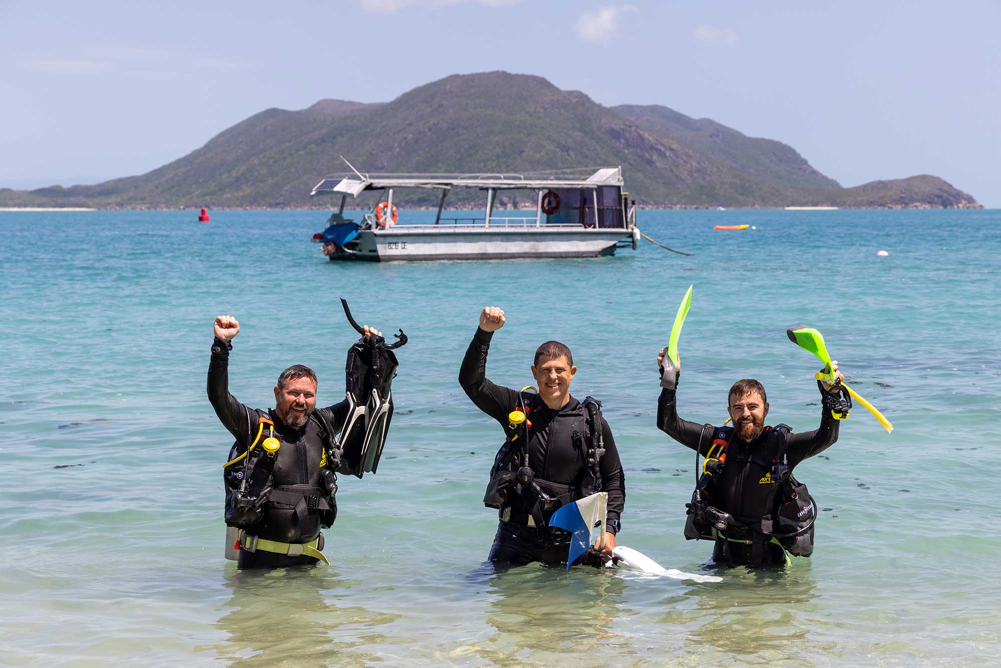 Three scuba divers waving off Fitzroy Island.