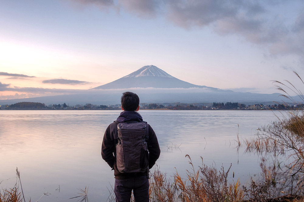 man wearing backpack looking out to view of mt fuji and lake