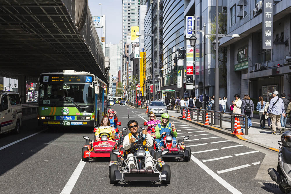 Tourists wearing costumes driving go-carts on a street in tokyo