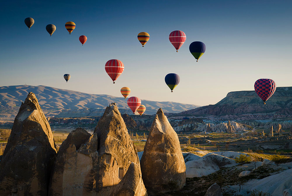 Hot air balloons rising over Cappadocia at sunrise.