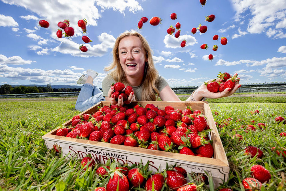 Young woman behind a tray of strawberries.