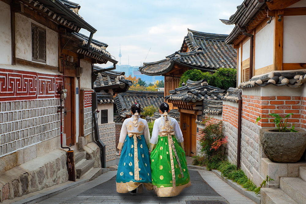 Back of two women wearing hanbok walking through the streets of Bukchon Hanok Village in Seoul.