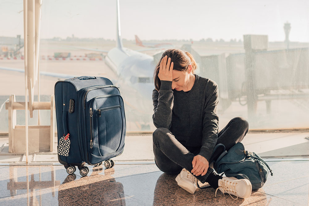 woman sitting on the floor next to her suitcase in an Airport having missed a flight