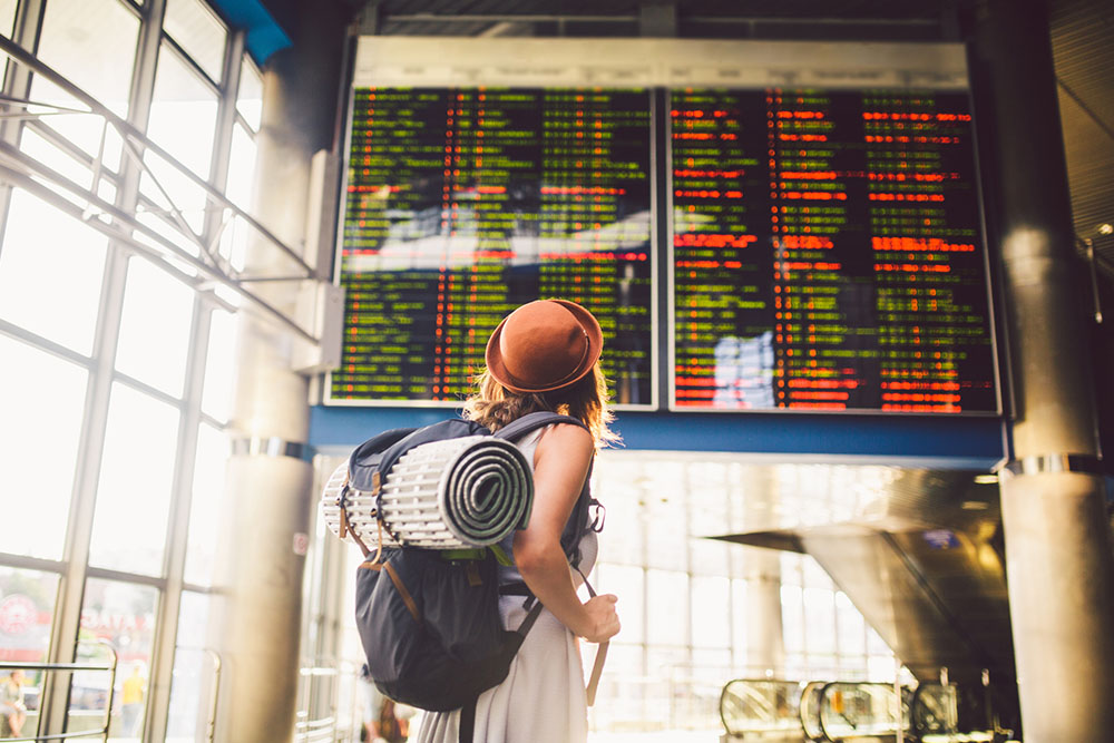Woman standing with her luggage looking up to view the airport schedule display
