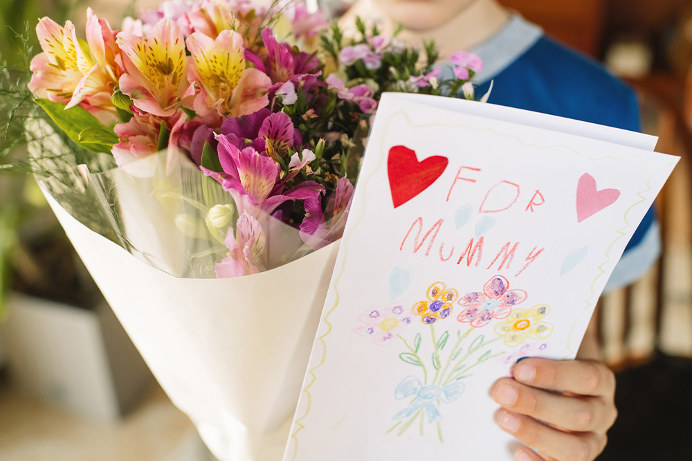Little-boy-with-flowers-and-greeting-card-for-his-mother-1000x666