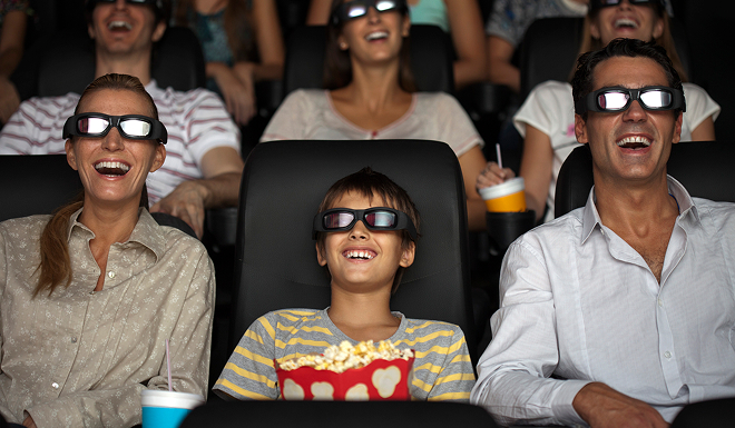 Family enjoying a movie together in a cinema, wearing 3D glasses and sharing popcorn during a family outing.