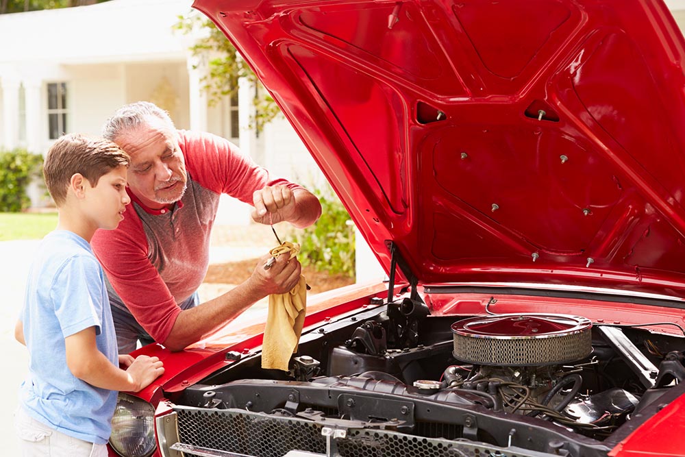Grandfather showing a grandson what is under the hood of a classic car