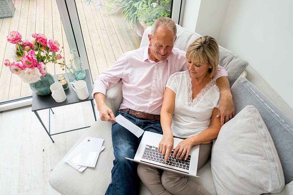 Middle aged couple at home on the couch using a computer and looking at bills