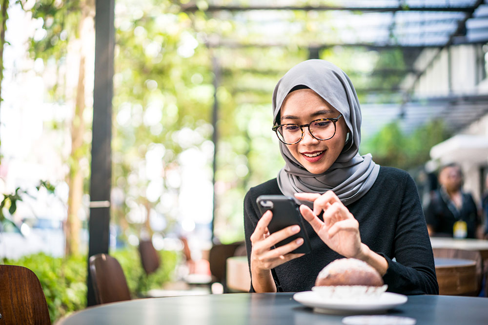 Woman in hijab using mobile phone outside a cafe