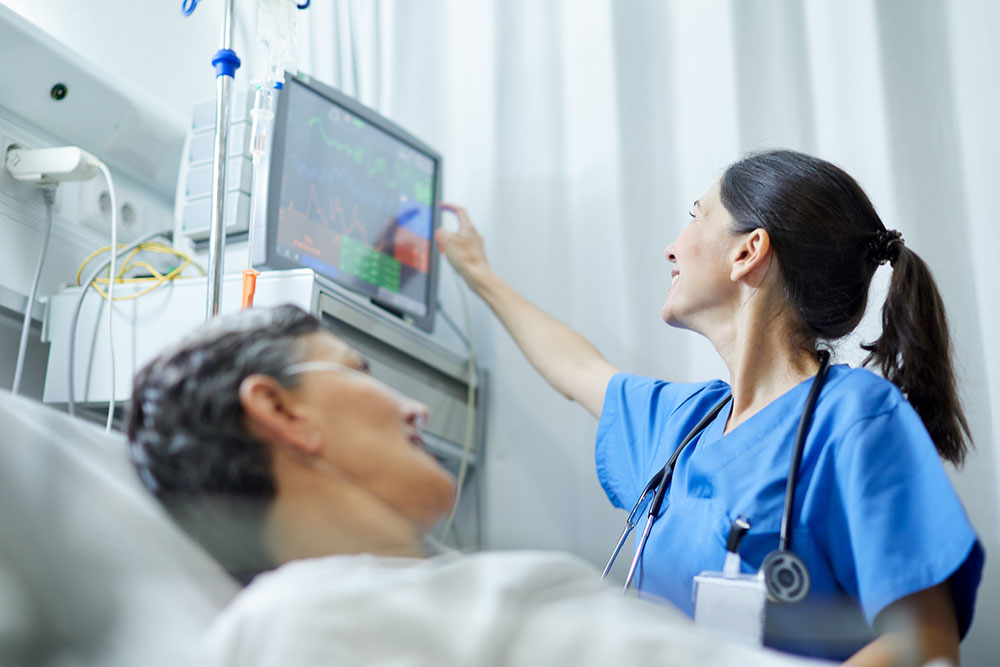 Woman lying in a hospital bed while a nurse checks a monitor