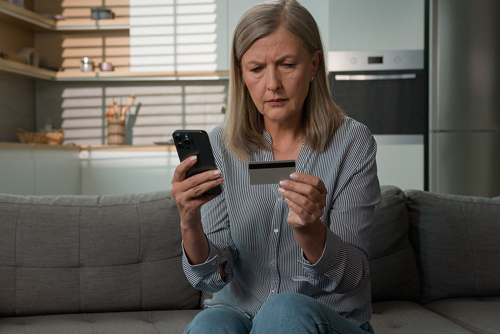 Worried woman looking at phone and credit card.