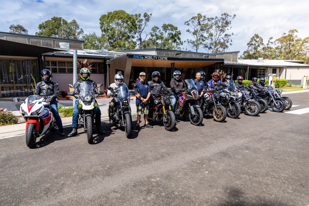 A group of people standing beside their motorbikes all iin a line.