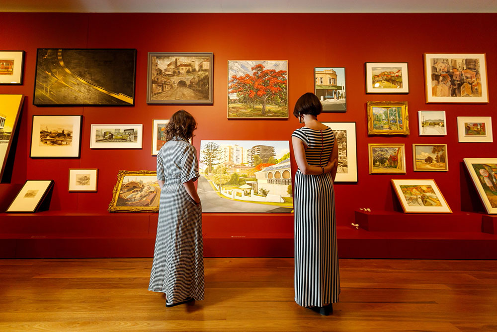 Two women viewing a wall covered in photographs depicting Brisbane