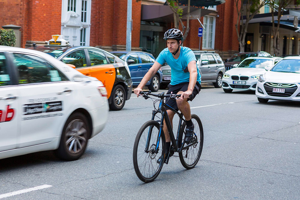 Male cyclist riding through a busy Brisbane city street.