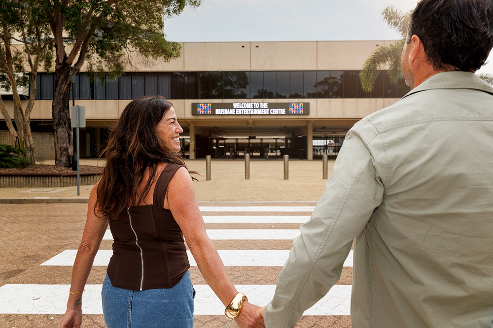 Man and woman holding hands walking towards Brisbane Entertainment Centre building