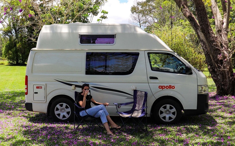 Woman sitting in a camping chair outside her Apollo van