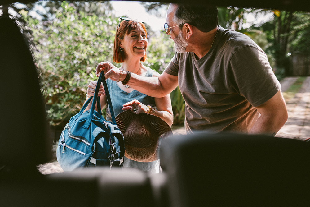 Middle-aged couple loading luggage into the bag of their car.