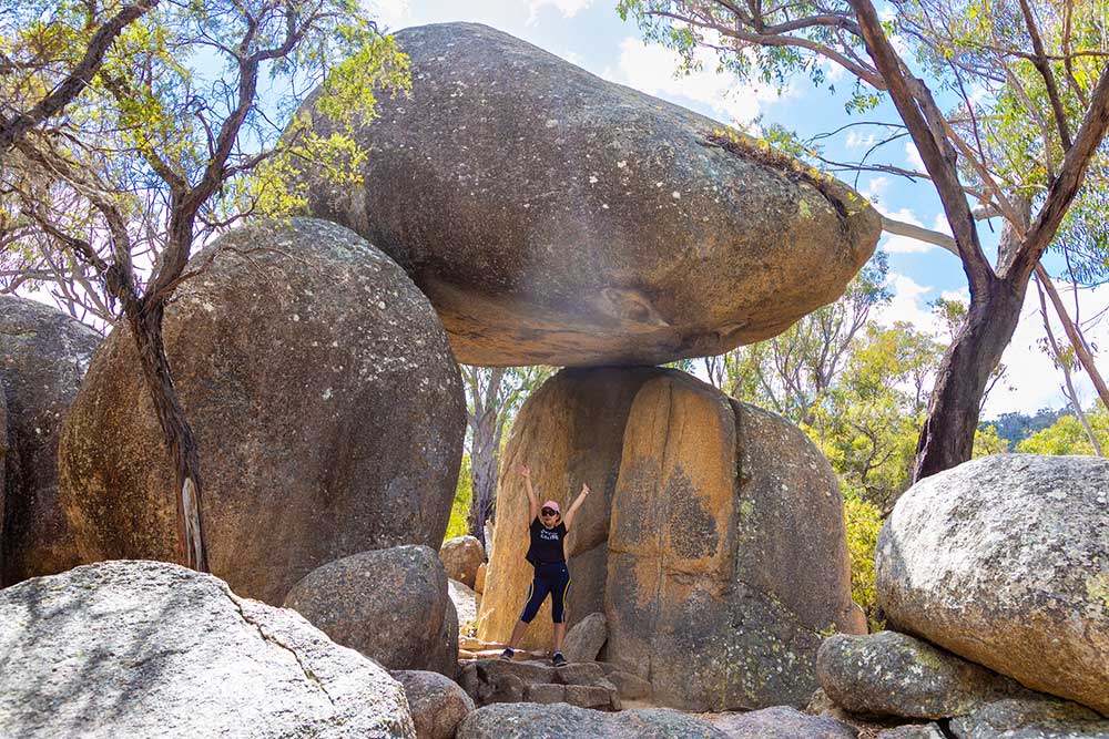 A woman poses for a photo under the Granite Arch rock formation in Girraween National Park