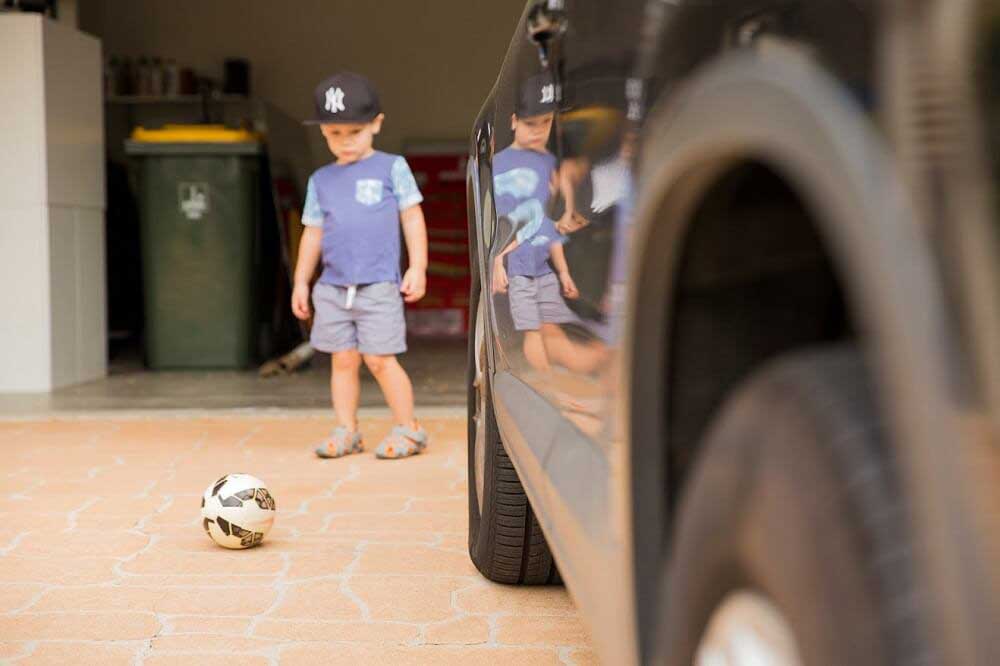 child playing in driveway next to car
