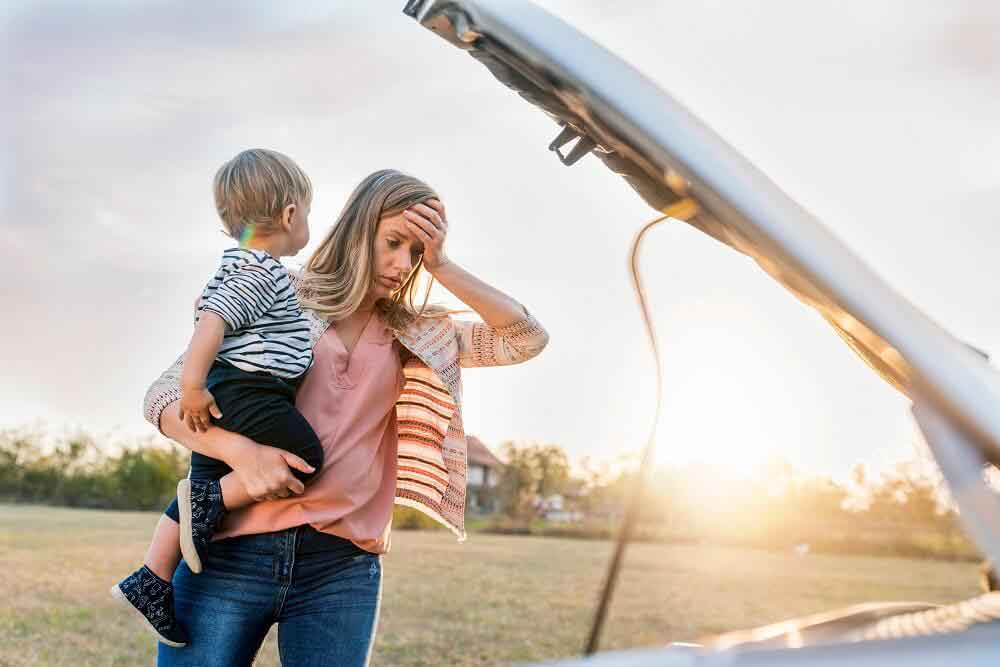 woman holding a child next to broken down car