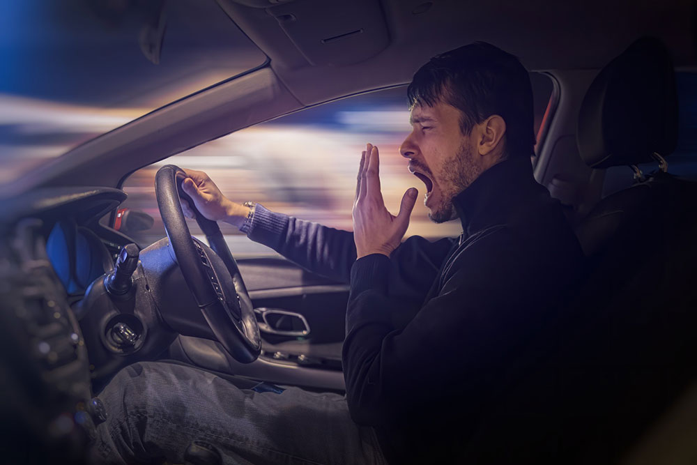 A tired driver yawns while behind the wheel.
