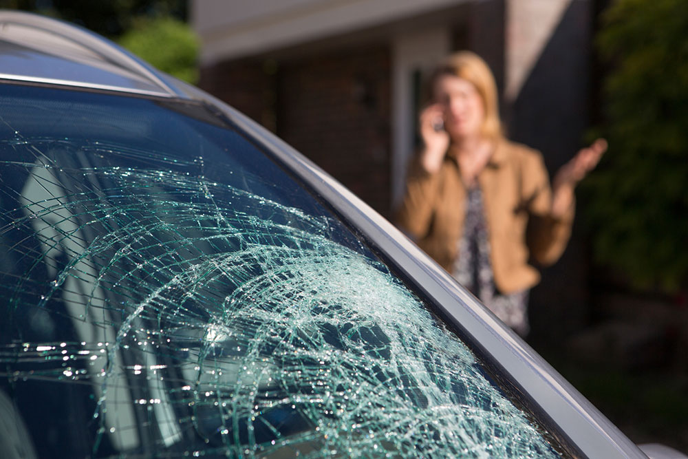 Woman on phone behind car with shattered windscreen.