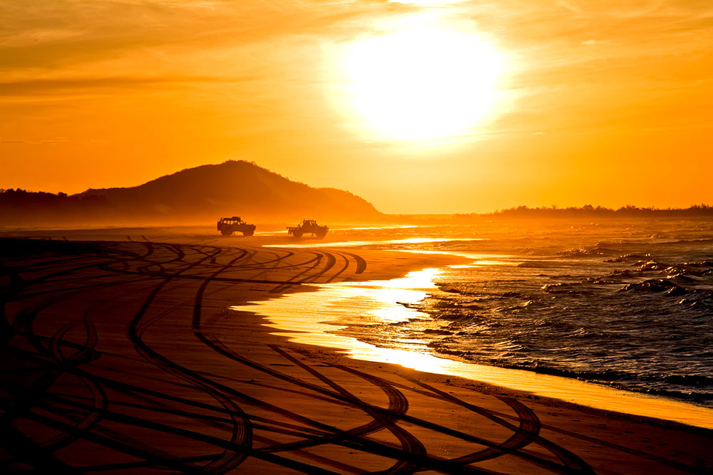 Two vehicles on a beach at sunset.