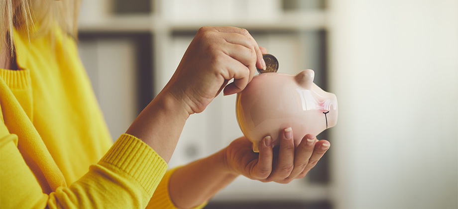 Woman in yellow putting coin in piggy bank