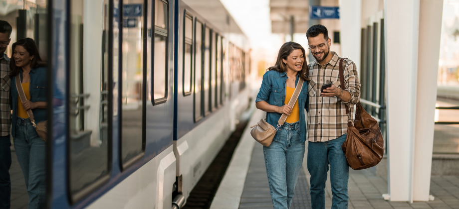 young couple using phone at train station while going on a trip overseas