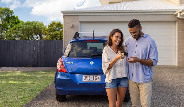 Happy couple standing in their driveway with car and keys