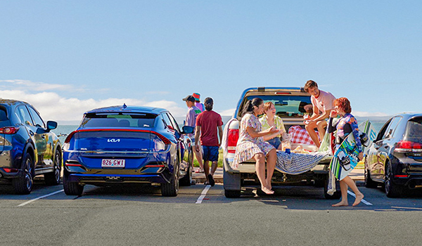 people at the beach in front of parked car 600x350