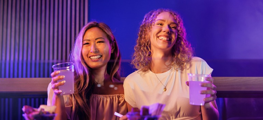 Two women smiling and holding drinks in the Brisbane Entertainment Centre while siting in VIP area