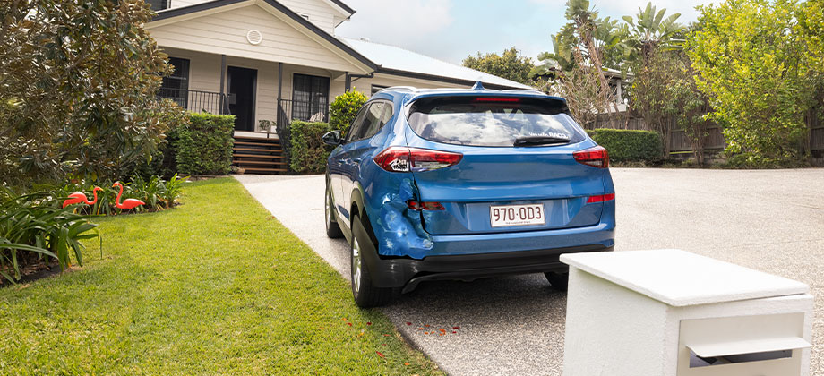 Blue car parked on a driveway with a dent on the rear bumper 