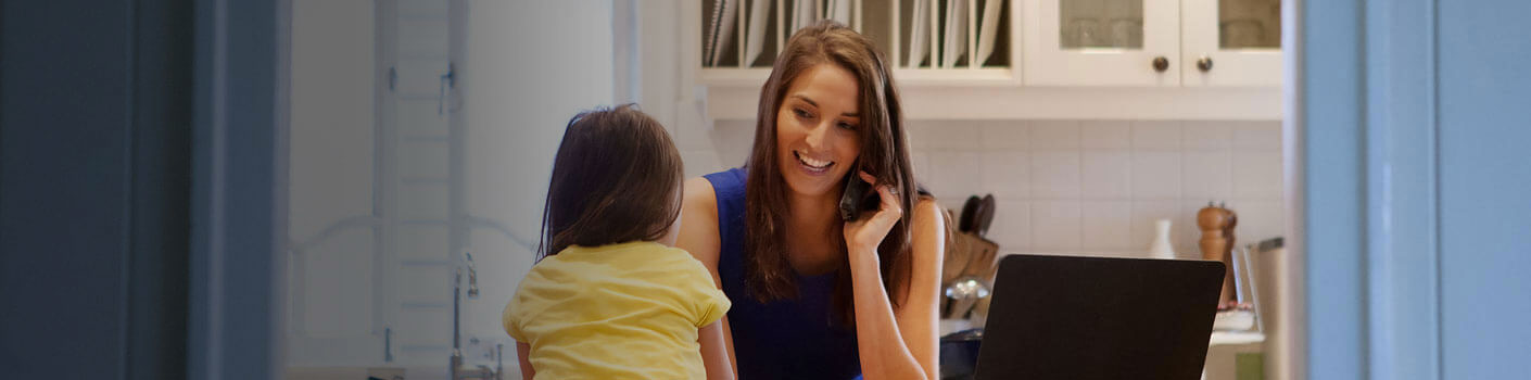 woman-with-phone-and-laptop-in-kitchen-smiling-at-daughter-1410x350