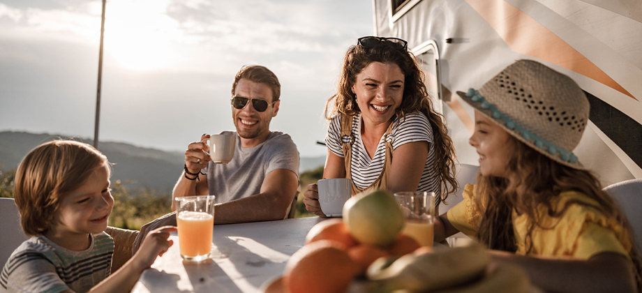family sitting outside caravan at table eating and laughing