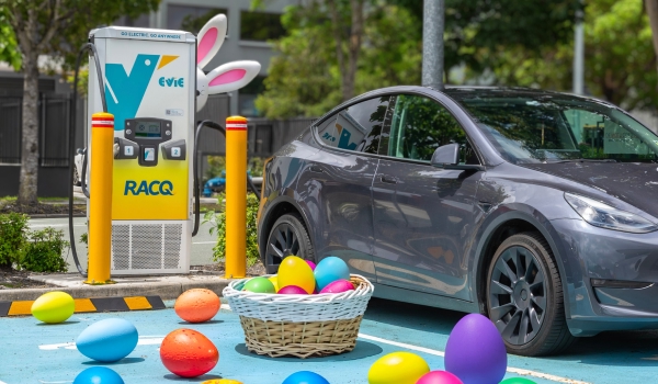 An Evie EV charger with white bunny ears next to a grey electric car, with colourful Easter eggs and a basket scattered in the parking bay