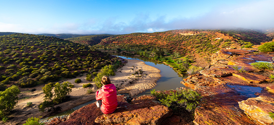 girl sitting on top of hill red rocks of kalbarri national park v2
